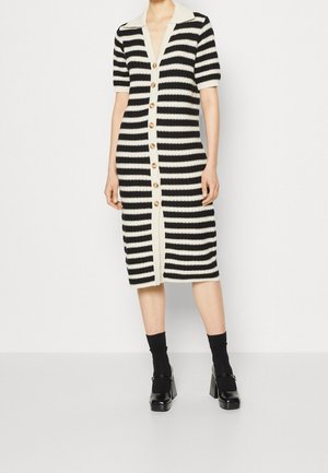 Woman wearing a black and white horizontal striped midi dress with buttons down the front, paired with black socks and platform heels.