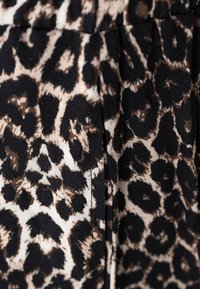 Luipaardprint stof met tan en bruine vlekken op een zwarte achtergrond; zachte textuur met een lichte glans; gedetailleerd patroon in verschillende vormen.