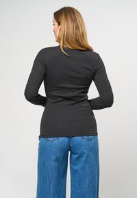Svart ribbad långärmad topp med en åtsittande siluett, bärs med lösa blå jeans. Texturen är mjuk och tyget har en lätt lyster.