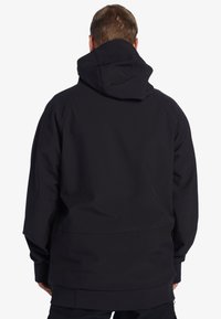 Čierna kapucňa s hladkým matným povrchom, so voľným strihom, nastaviteľnou kapucňou a ribbovanými manžetami na zápästiach a leme.