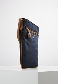 Borsa in nylon blu con dettagli in pelle color cuoio, design slim, chiusura con zip superiore, tasca frontale con zip e hardware color oro. Misura circa 30 cm in altezza.