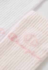 Dos pares de calcetines acanalados, uno blanco y otro rosa claro, cada uno con un sutil diseño de logo en rosa. Textura suave, de longitud media hasta la pantorrilla.