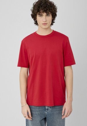 T-shirt en coton rouge à manches courtes, col rond, et coupe droite. Présente des coutures discrètes et un petit logo près de l'ourlet.