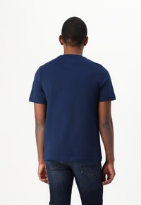 Mørkeblå t-skjorte med korte ermer laget av myk bomull, med rund hals og en avslappet passform, kombinert med mørke denim-jeans.