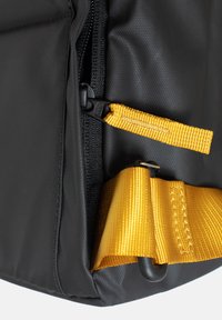 Angolo di una borsa nera in tessuto con una cerniera e una tracolla. Presenta una vivace fettuccia gialla con dettagli di cucitura e una robusta clip in plastica.