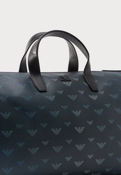 Σκούρο μπλε τσάντα tote σχεδιασμένη με επαναλαμβανόμενα ανοιχτό μπλε αφηρημένα λογότυπα αετού και μαύρες δερμάτινες λαβές.