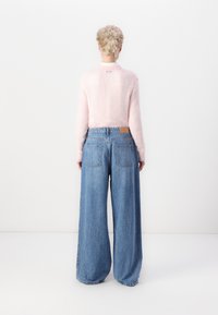 Suéter fuzzy rosa claro combinado con jeans de mezclilla azul de pierna ancha. El suéter tiene un cuello alto; los jeans tienen un lavado desgastado y bolsillos traseros.