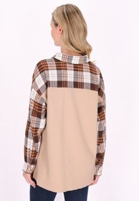 Cămașă din flanel cu un model în carouri în nuanțe de brun, portocaliu și crem. Partea inferioară este dintr-un material ribbed solid bej. Guler clasic și mâneci lungi.