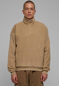 Beige fleece half-zip genser med høy krage, nedre skuldre og ribbede mansjetter. Myk tekstur og avslappet passform, parret med matchende bukser.