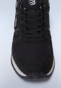 Sneaker nera con una combinazione di suede e tessuto, lacci neri, accenti argento e una suola in gomma testurizzata.