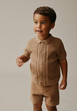 Strick-Zweiteiler in sanftem Beige mit einem kurzärmeligen Oberteil mit Kragen und Knöpfen sowie passenden Shorts, die strukturierte Muster betonen.