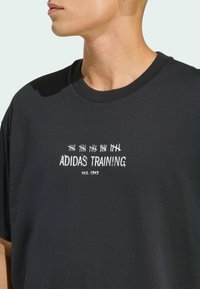 Schwarzes Baumwoll-T-Shirt mit Rundhalsausschnitt, auf der Vorderseite mit weißem gesticktem Text "ADIDAS TRAINING" und "est. 1949". Einfaches Design.