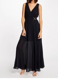 Svart maxiklänning med V-ringning, plisserad byst och en figursydd midja med ett bälte i guldton. Genomskinlig maxikjolsöverdel.