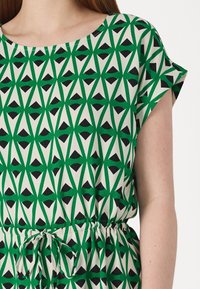 Green and black geometric patterned dress with short sleeves, cinched waist, and a round neckline. Made from lightweight fabric.