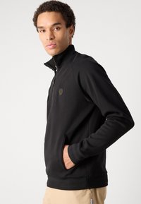 Giacca nera a pullover con colletto a mezza zip, tasche laterali, polsini a costine e orlo. Presenta un logo discreto sul petto. Tessuto morbido.