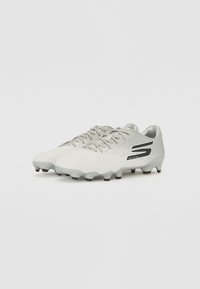 Crampons de football blancs avec une finition texturée, des accents gris et un logo noir. Présentent un design à lacets et des crampons multidirectionnels pour une traction optimale.
