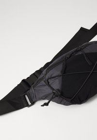 Schwarz und grau Taillentasche aus strukturiertem Nylon, mit einer zentralen Reißverschlusstasche und einem verstellbaren Gurt mit Schnellverschluss.