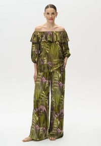 Top floral off-shoulder con cuello rizado en verde y morado, combinado con pantalones de pierna ancha que presentan un patrón a juego y un ajuste holgado.