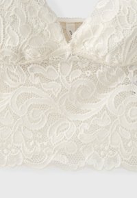 Bralette en dentelle blanche avec motifs floraux et tourbillonnants et un petit détail ruban au centre devant.