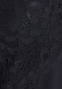 Tissu noir avec un motif complexe de dentelle florale comprenant différentes formes de feuilles et des coutures texturées.