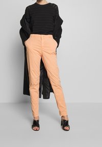 Svart texturerad långärmad topp, ljusorange slim-fit byxor och öppna svarta klackar med nitar.