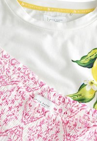 Valge topp, millel on suur sidruni ja lehe trükk; alumine osa on kaunistatud roosade smock-immitustega, millel on lillemustrid. Etiketil on kirjas "b by Ted Baker."