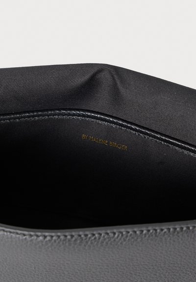 Εσωτερικό μαύρης τσάντας με απαλή υφή σατέν, διακοσμημένο με διακριτικό λογότυπο σε χρυσό. Οι άκρες έχουν ραφτεί προσεκτικά για ανθεκτικότητα.