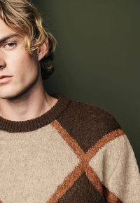 Brown and cream argyle-patterned sweater with a ribbed neckline and textured fabric, featuring contrasting diamond shapes in shades of brown.