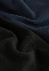 Dos capas de tela suave: una de un negro intenso y la otra de un azul marino oscuro. Ambos materiales tienen una textura lisa con suaves pliegues y arrugas.