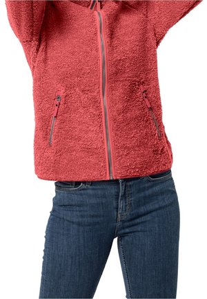 Rode fleecejas met ritssluiting aan de voorkant en met ritssluitingen afgesloten zakken, gedragen met een blauwe spijkerbroek, persoon die de armen boven het hoofd heft.