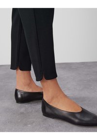 Svarta skräddarsydda byxor med en texturerad yta, prydda med en subtil vågig fåll. Matchas med eleganta svarta läderskor.