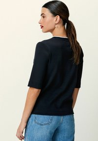Marineblå kortærmet top med rund halsudskæring, ribbede manchetter og kant. Sammen med lyseblå jeans. Glat tekstur og tætsiddende design.