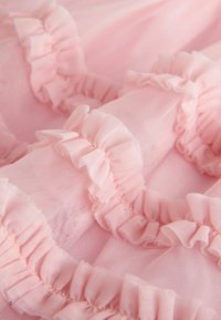 Vaaleanpunainen tylli, jossa on röyhelöitä reunoilla, kevyt, pehmeä rakenne ja hienostunut läpikuultava ulkonäkö.