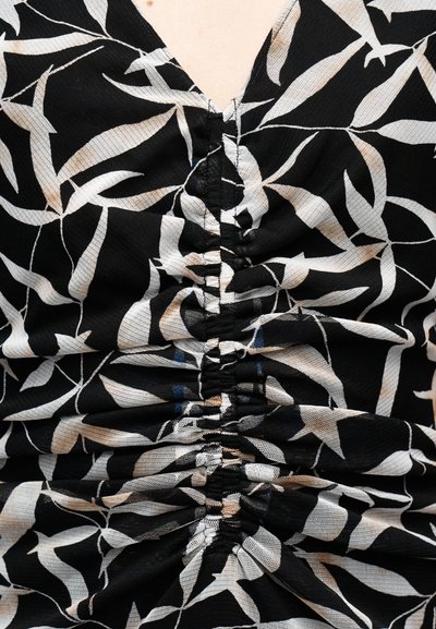 Μαύρο ύφασμα με λευκά και μπεζ φύλλα, με ραφή που συγκεντρώνεται και τρέχει κατακόρυφα στο κέντρο του ενδύματος.