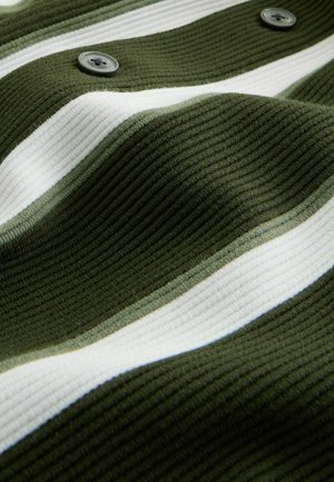 Groen ribstof met witte strepen. Twee grijze knopen zichtbaar. Golvende textuur die de zachtheid en structuur van het materiaal benadrukt.