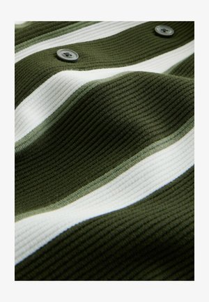 Zeleni rebrasti materijal s bijelim prugama. Dva siva dugmeta su vidljiva. Valovita tekstura naglašava mekoću i strukturu materijala.