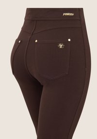 Leggings marrones hechos de material suave, con acentos dorados y costuras. Incluyen un logotipo en la cintura y dos bolsillos traseros.