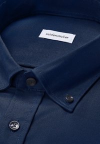 Marineblauw overhemd met knopen en een geknoopte kraag, met een wit label in de hals dat "seidensticker" leest.