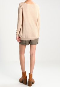 Ljusbeige stickad tröja med ett strukturerat mönster, tillsammans med olivgröna shorts. Bruna ankelskor med robusta klackar.