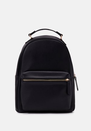 Sac à dos noir avec poche zippée à l'avant, poignée supérieure et design arrondi sur fond blanc.