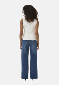 White sleeveless top with a lace V-neckline, paired with high-waisted wide-leg blue jeans, featuring back pockets and a frayed hem.