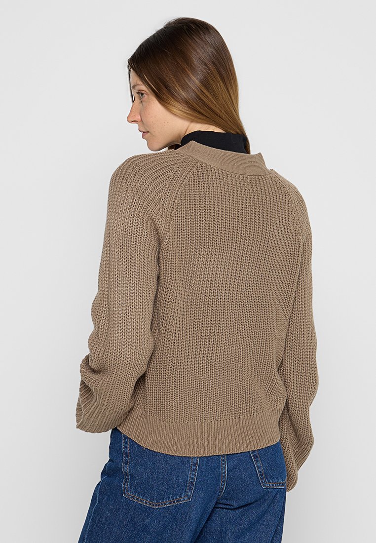 Brauner Strickpullover mit geripptem Kragen und Bündchen. Verfügt über eine strukturierte Oberfläche und einen taillierten unteren Saum. Getragen mit blauen Denim-Hosen.
