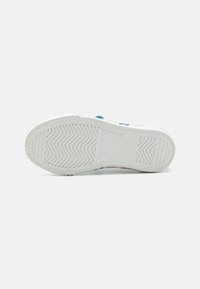Semelle de sneaker blanche avec un motif de traction texturé, featuring des accents bleus et du texte multicolore imprimé sur le côté. Matériau en caoutchouc lisse.