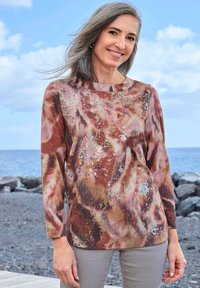 Langsleeve top in tinten van roest, crème en bruin met abstracte patronen; zachte stof; ronde hals; aangevuld met lichtgrijze broek.