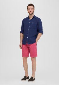 Chemise en lin bleu marine à boutons et manches retroussées, associée à un short en coton rose. Complétée par des chaussures noires à enfiler. Design simple et décontracté.