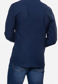 Camisa de manga larga azul marino con textura suave, cuello abotonado y dobladillo curvado, combinada con vaqueros azules que cuentan con un diseño clásico de cinco bolsillos.