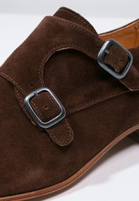 Scarpa in suede marrone con design a doppia fibbia e soletta in pelle liscia. Presenta una punta tonda e un tacco in legno basso.