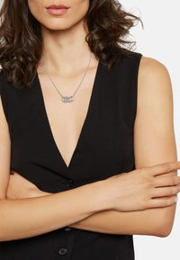 Sølv halskæde med fire sammenkoblede ringe, båret af en model. Halskæden har en delikat kæde og hviler over en dyb V-udskæring.