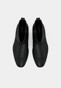 Pár čiernych kožených členkových čižiem so bočnými zipsami a úchytkami, zobrazených zhora na bielom pozadí.