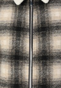 Plaid zip-up striukė su juoda, pilka ir kreminės spalvomis, pagaminta iš storesnio, tekstūruoto audinio su minkštu, flisinio tipo apykakle.